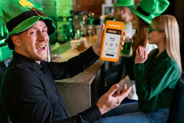 Bartender holding an easyPayments easyPro card machine in a pub on St. Patrick's Day