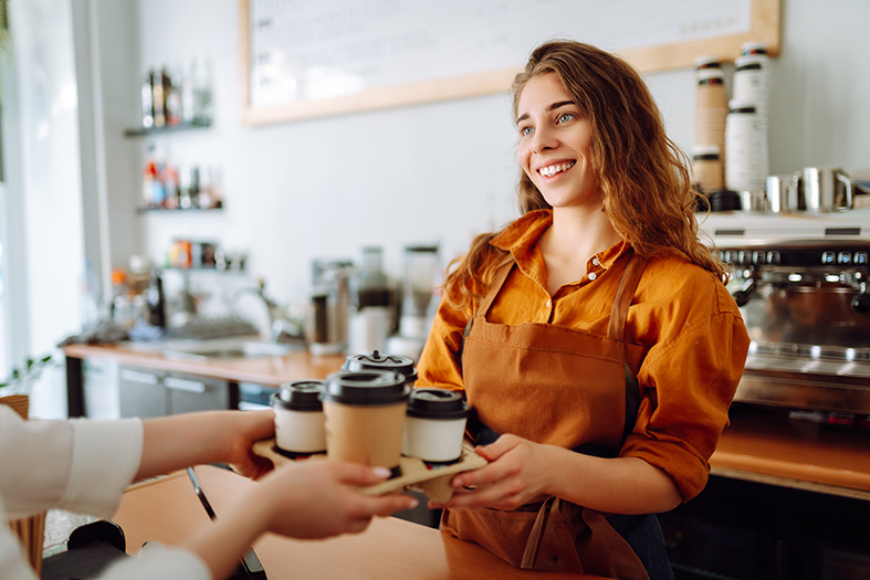 Female barista handing a takeaway coffee to a customer at an Irish coffee shop using card payments